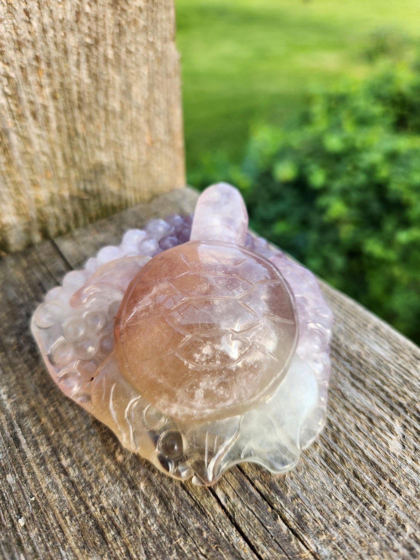 May include: A carved crystal turtle figurine with a pink and purple color gradient. The turtle is sitting on a wooden surface.