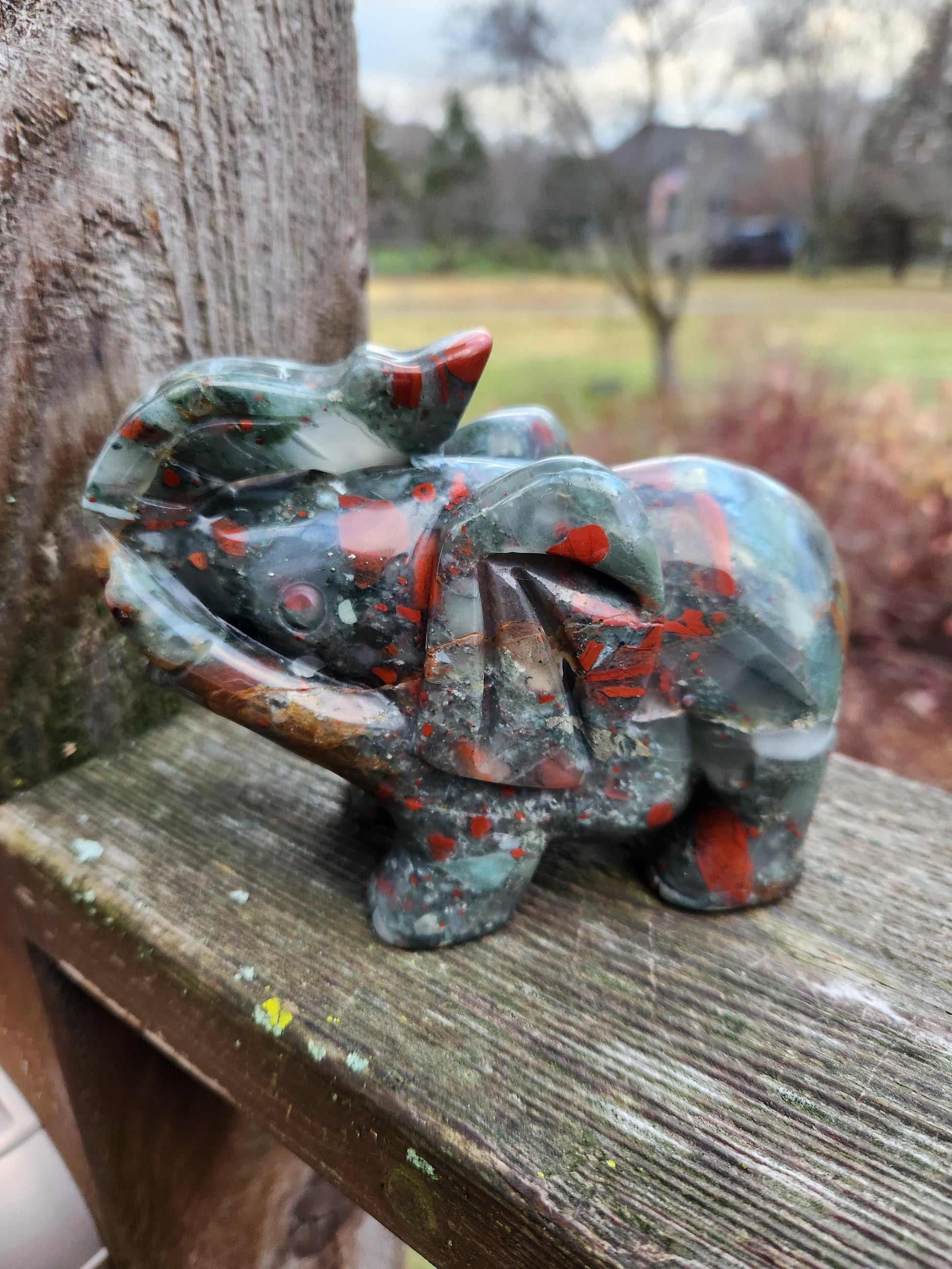 May include: Intricate carved elephant figurine crafted from polished red and green jasper stone. The elephant&#39;s detailed features and vibrant color variations are showcased. This collectible piece is perfect for adding a touch of nature-inspired artistry to any space. The smooth, polished surface of the stone enhances the rich colors and intricate details of the carving.