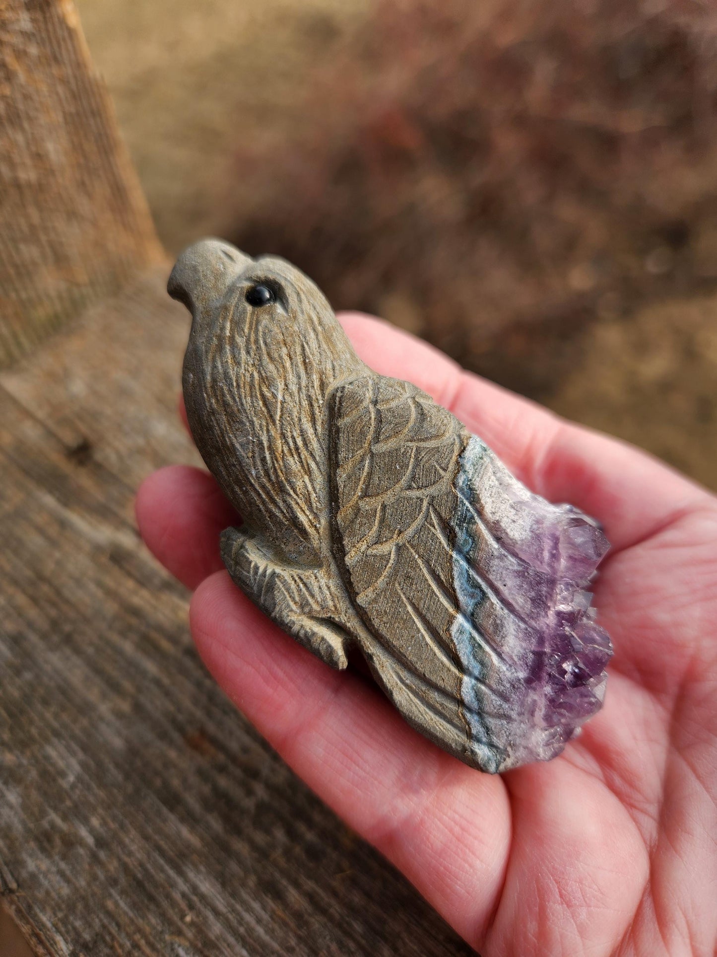 May include: A carved eagle figurine made of amethyst with a purple and gray color scheme. The eagle is perched with its wings spread and has a detailed carving of its feathers.